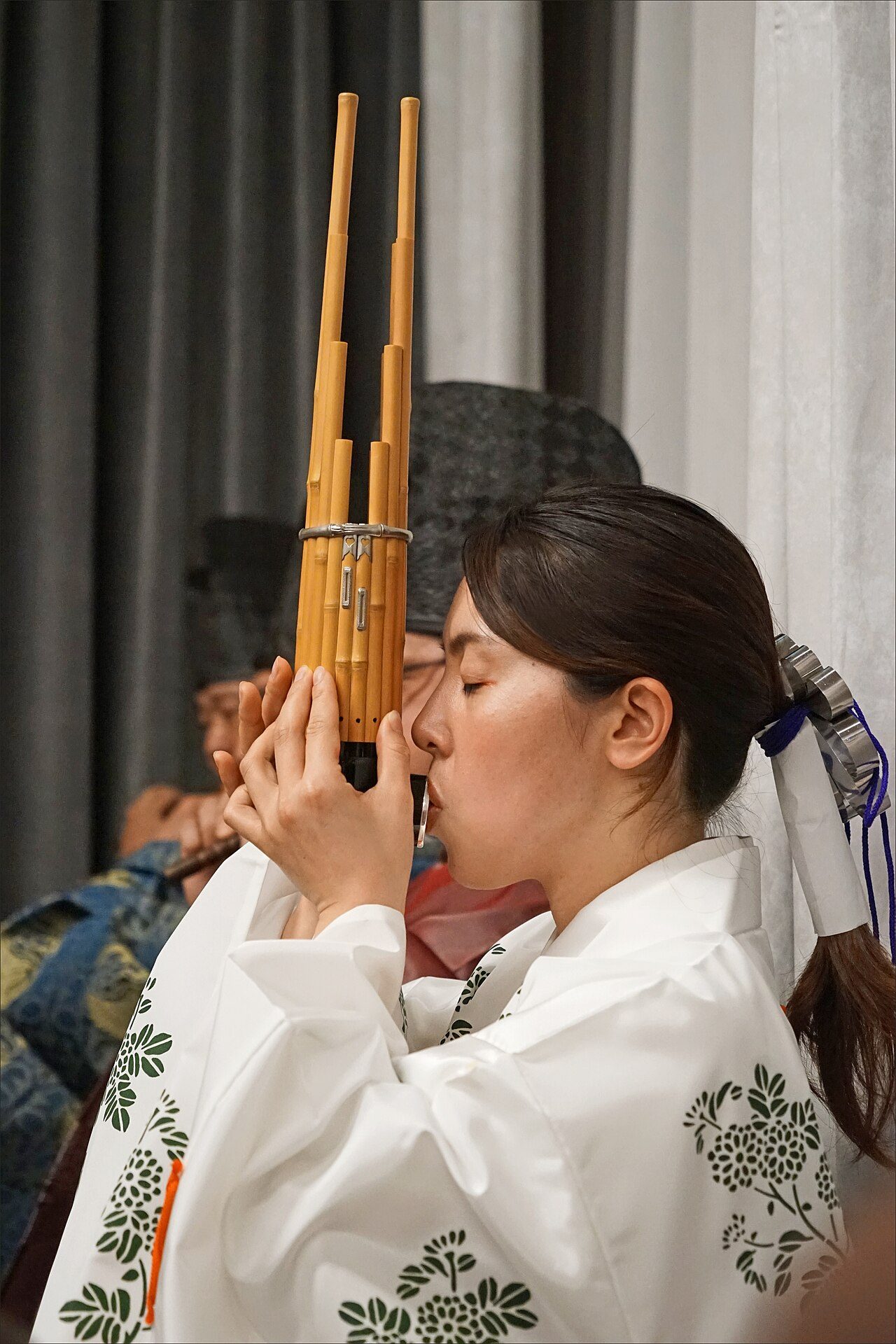 Musicienne jouant du shô de l'ensemble de Gagaku "Owari Miyabie. Au premier plan : joueuse de Shô, orgue à bouche, cette musicienne de Gagaku est également danseuse de Bugaku. Concert dans le grand salon de la Maison du Japon Cité Internationale Universitaire de Paris (CIUP)…