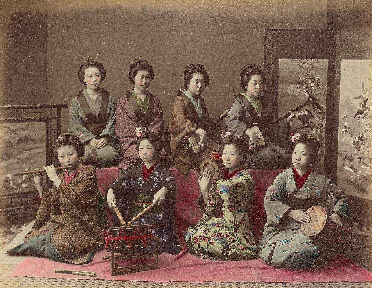 In this photograph taken by Kusakabe Kimbei , eight women are pictured. Six of the women are playing traditional Japanese instruments, including the Samisen, Tsudzumi, Fuye and Taiko; the other two strike a pose. This photograph was originally a silver albumen print without…