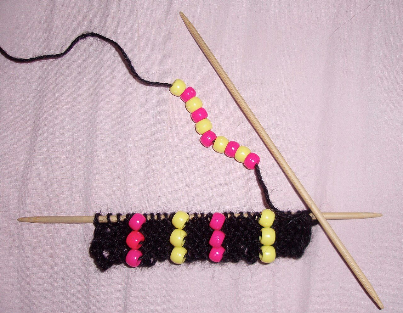 picture of bead knitting- black wool, pink and yellow beads, knitted on double points