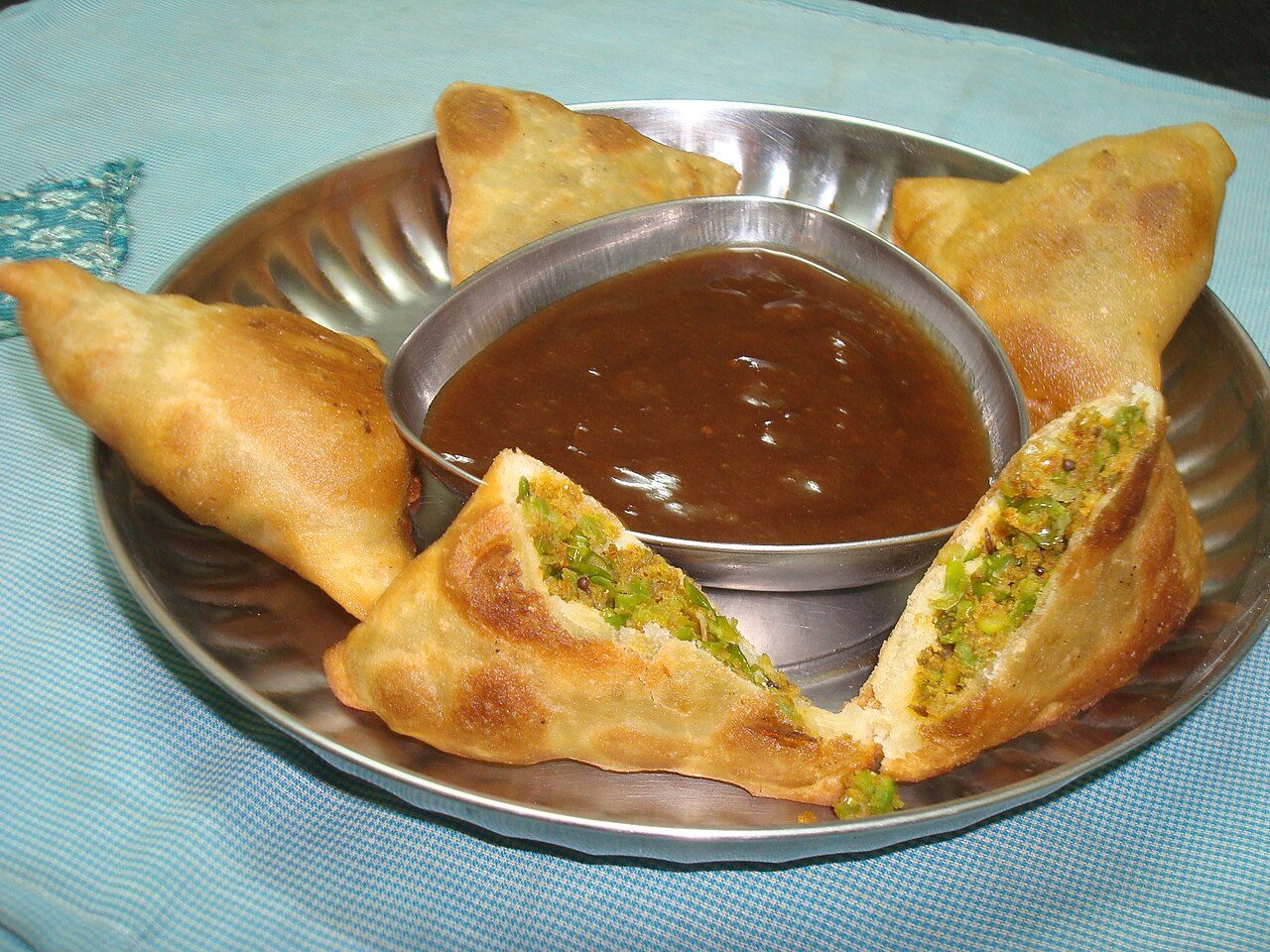 Green peas filling in samosas with tamrind chutney in center.
