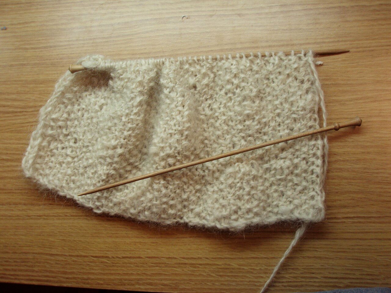 A picture of a scarf being knitted on single point needles out of homespun yarn