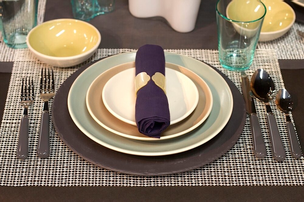 Table-setting for a multi-course meal, including placemat, charger plate, napkin with napkin ring, and drinking glass.
