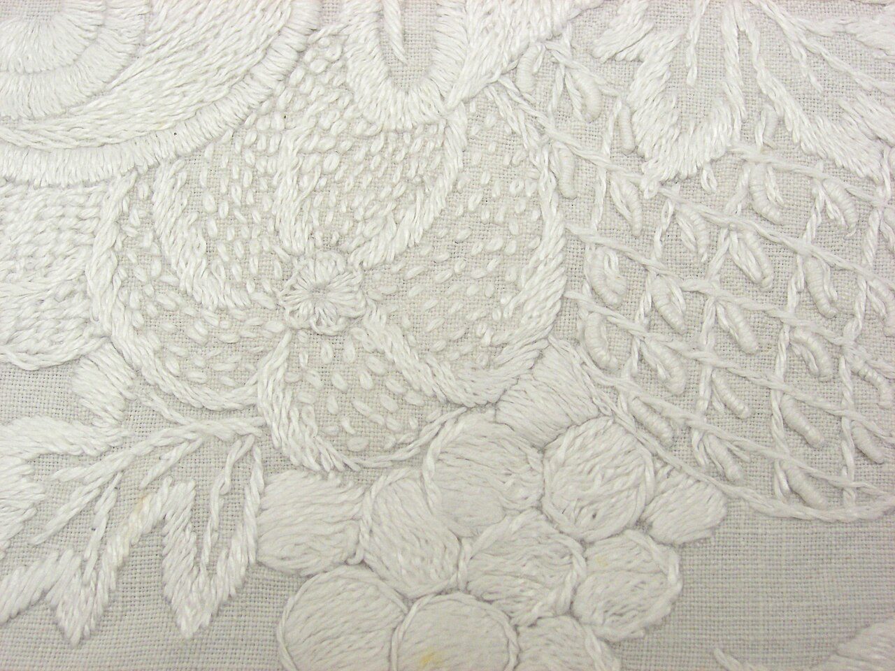 Long white linen table runner with (crochet) lace border, the symmetrical design worked in Mountmellick work including bullion and stem stitches. Design comprising a central shield-like device containing the monogram "BT" from which to either side runs an undulating vignette…