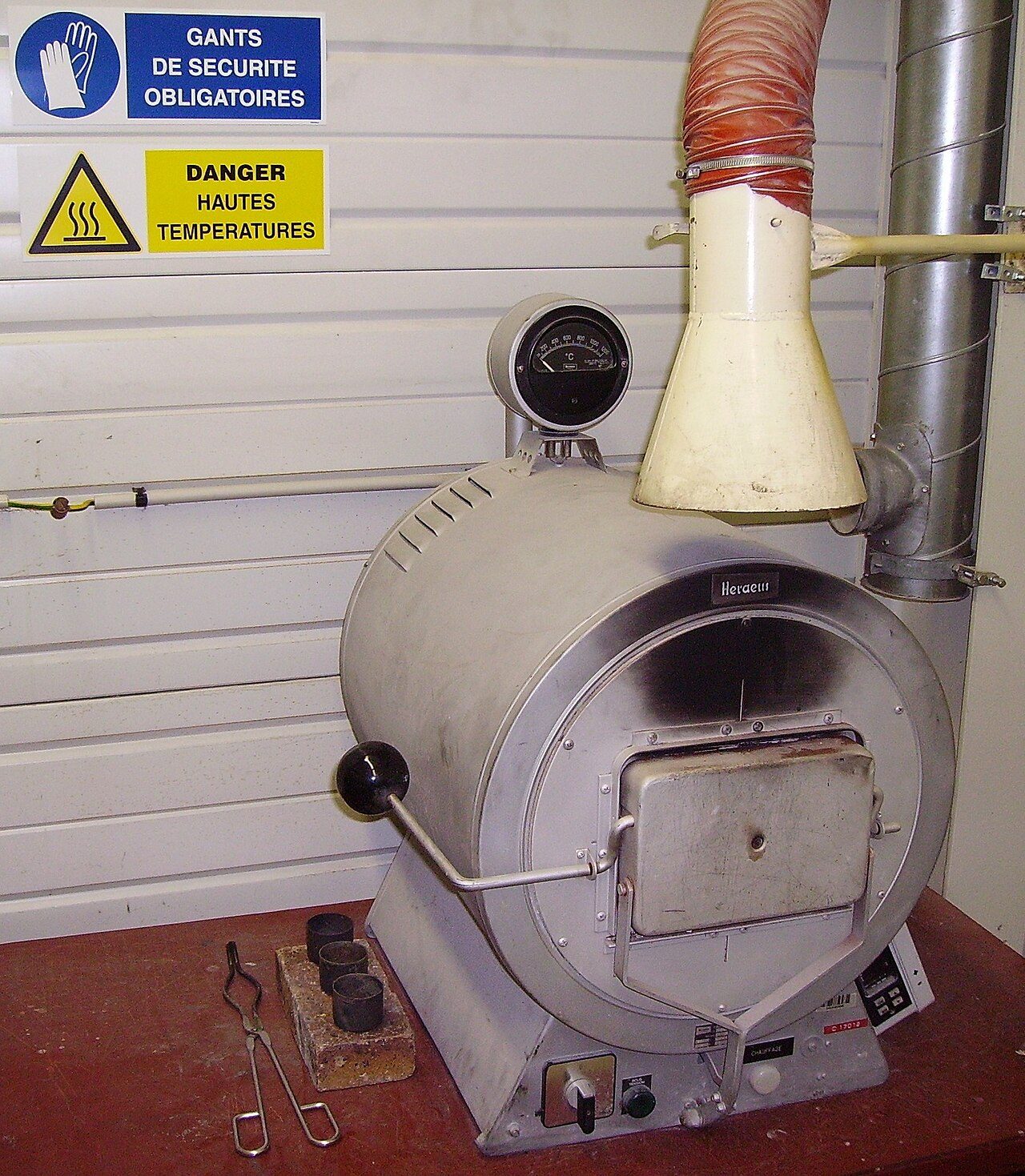 Laboratory muffle furnace Heraeus model KR 170. Maximum temperature: 1 150 °C; 14 A, 24 electrical resistances. Three metal crucibles and tongs are visible. Used for calcination, ash content…