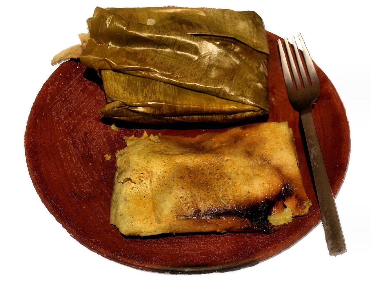 Photo of wrapped and unwrapped Tamales Oaxaqueños. The tamales consists of masa, chicken and mole negro, wrapped in plantain leaves. Taken in Oaxaca, Mexico.