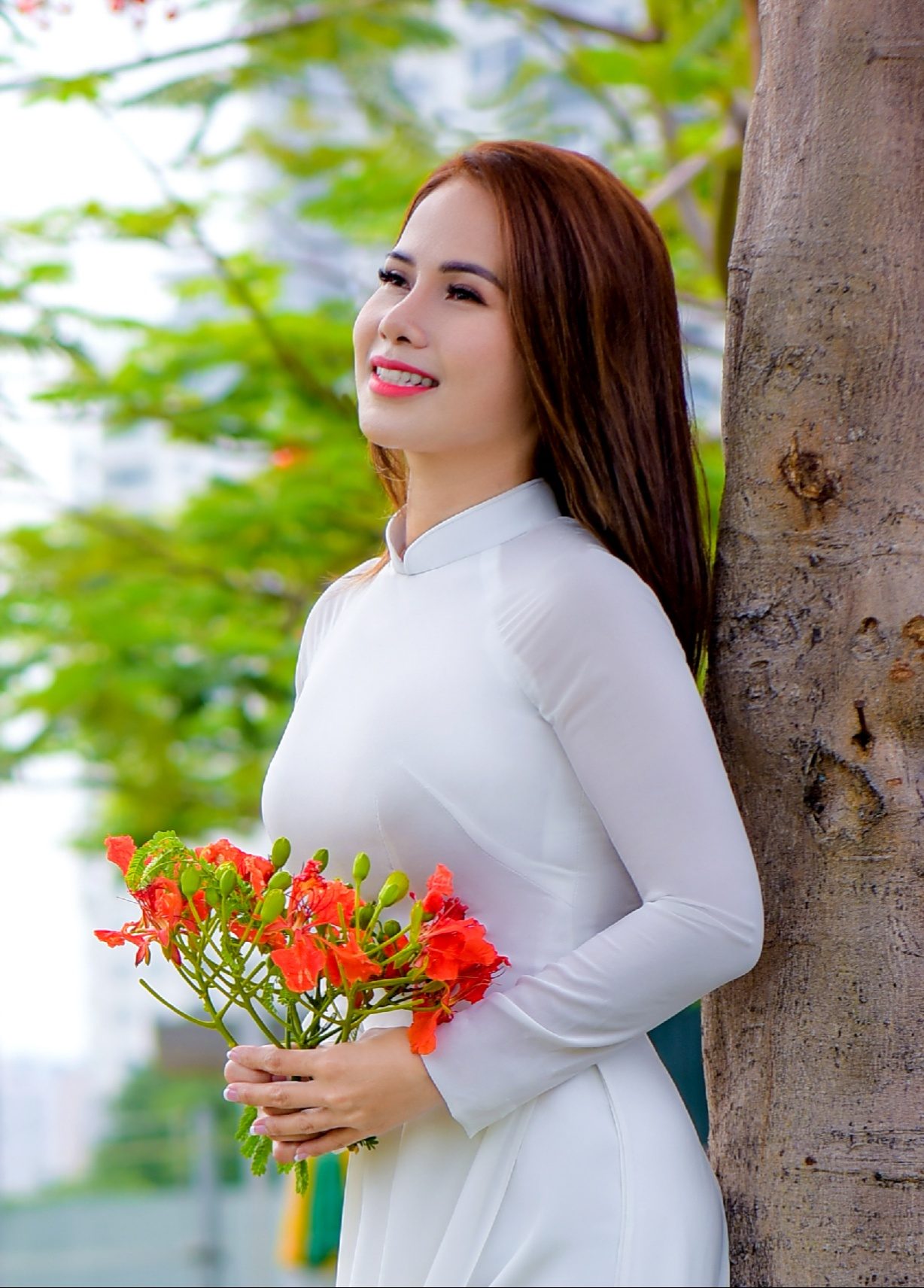 Cô gái ở TP. Hồ Chí Minh mặc áo dài, trên tay cầm hoa phượng đỏ.