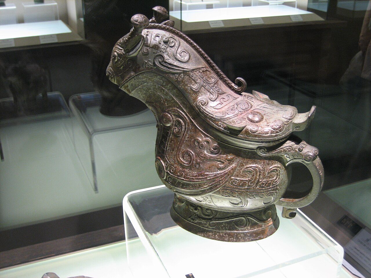Gong Fu Yi . A bronze animalistic Chinese gong vessel , 13-11 century B.C., late Shang Dynasty , Shanghai Museum . The head has rabbit ears and giraffe horns, and the shine looks like a small dragon in high relief. The back of the cover has the shape of the head of an ox, like…