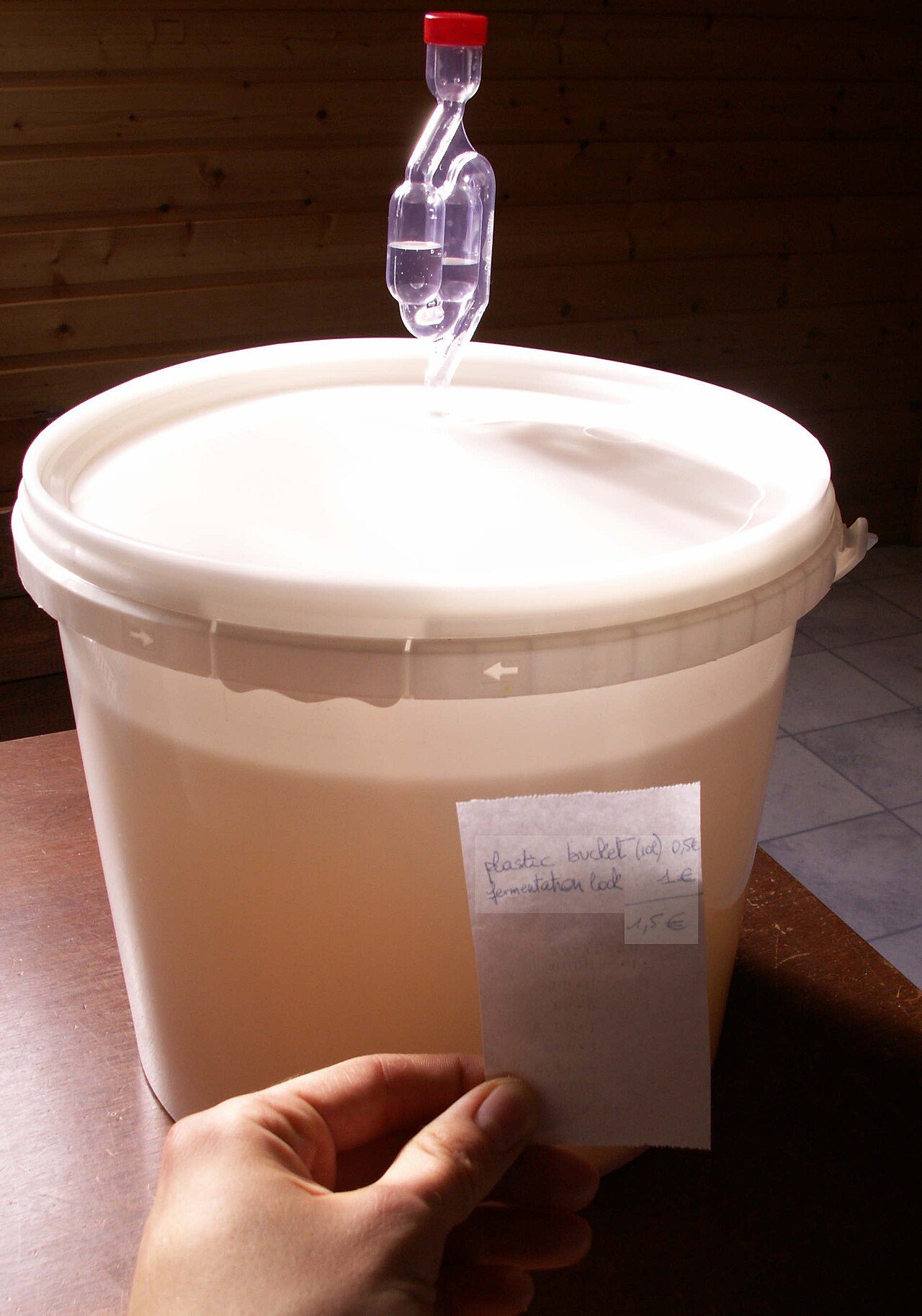 A picture of a cheap fermentation vessel (regular plastic buckets of 10l) with integrated fermentation lock (by drilling a hole inside the bucket and inserting the locke herein). The whole costs but 1,5 € where a demijohn with lock and sealing rubber may easily cost 30-35€. The…