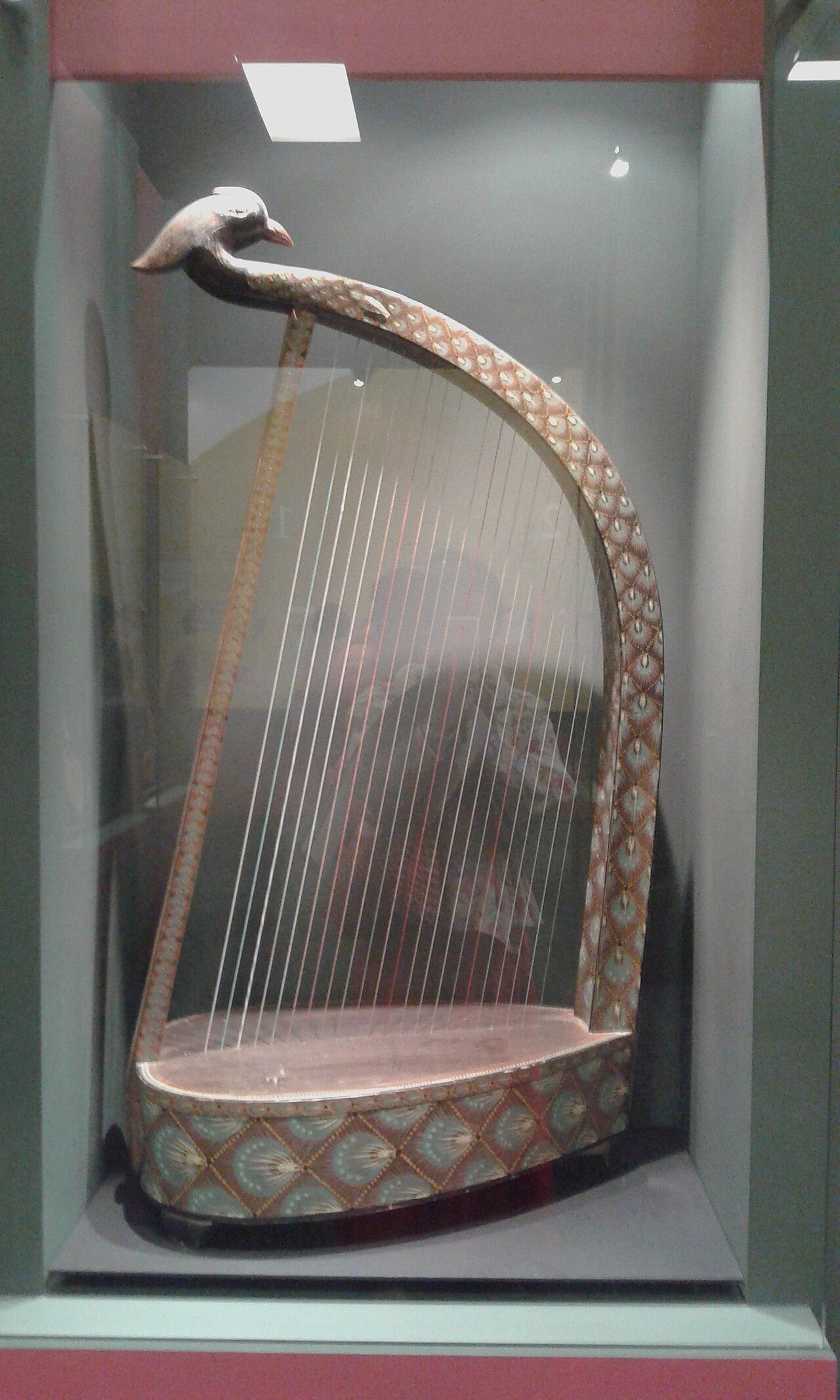 Phoenix-headed konghou (a type of harp), Tang dynasty (618-907). Base is an egg-shaped-prism soundbox, neck arches over it and then recurves, the end carved in a bird head. Painted all over with a pattern of brown-edged pale green feathers between squares outlined in yellow…