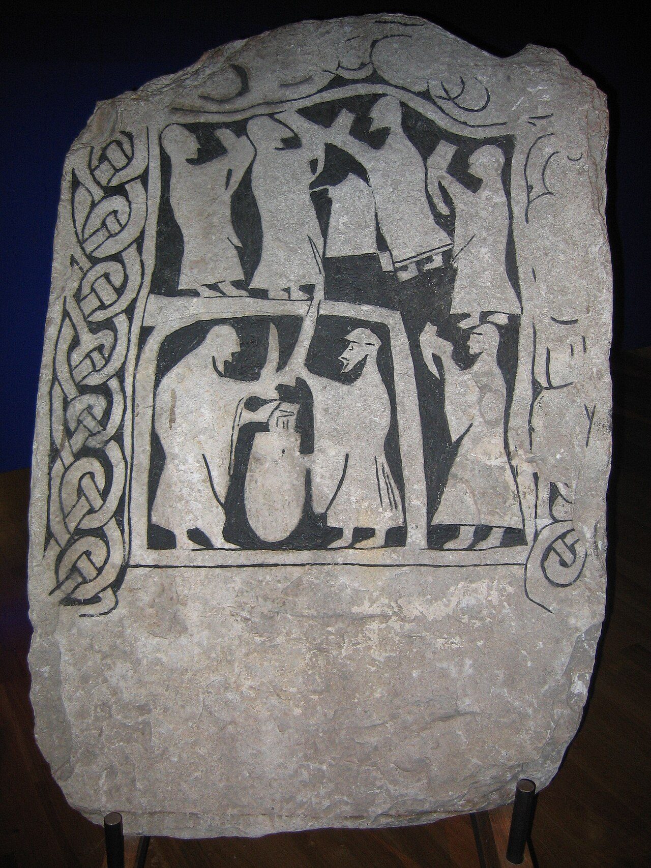 Picture stone depicting a drinking scene. Seven figures with long robes with long sleeves stand together, all of whom hold drinking vessels in their hands. Two of the figures stand in an enclosure around a vat or cauldron with their drinking vessels upended as if they might be…