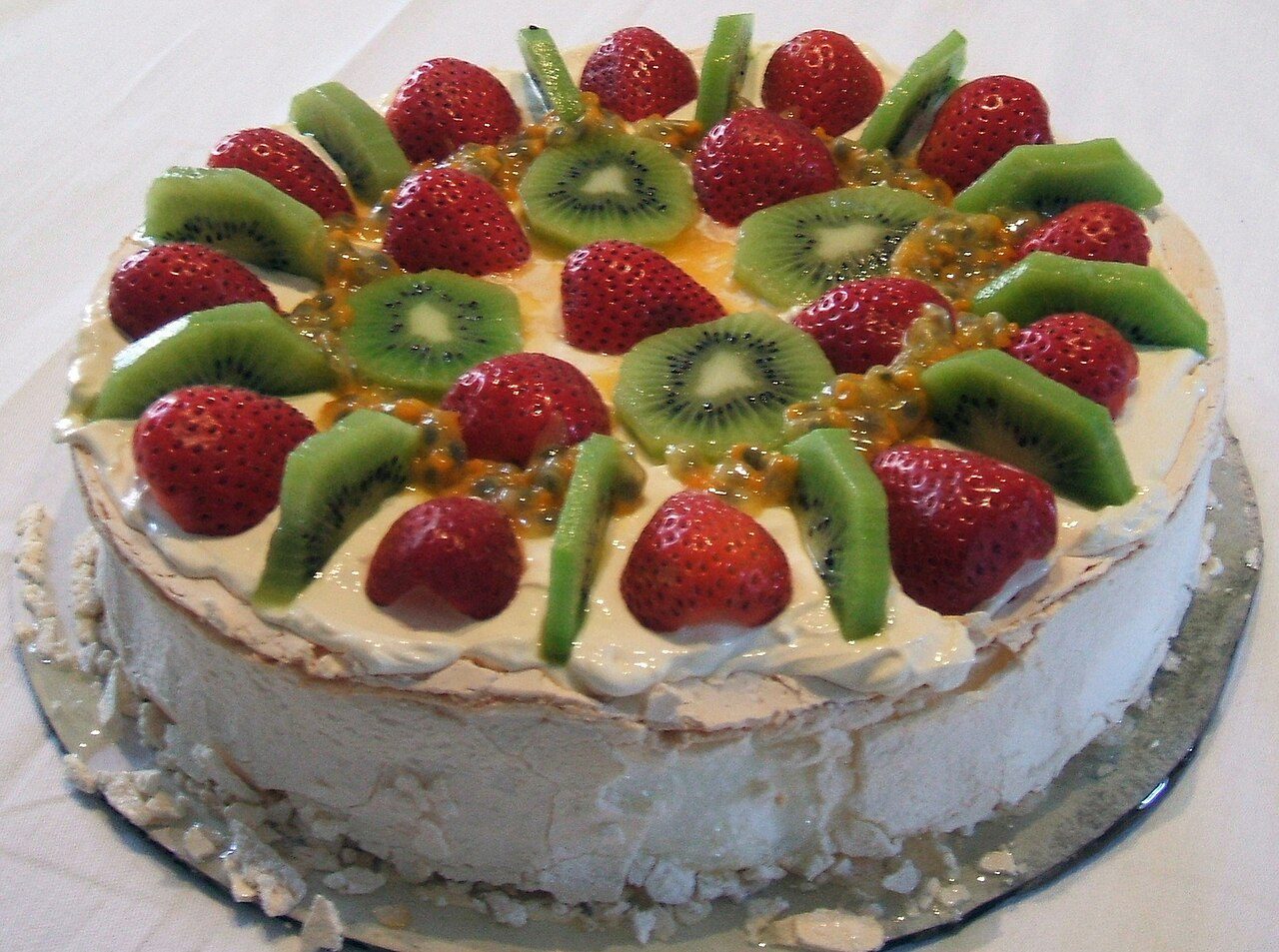 Photo of pavlova dessert with topping of kiwifruit, strawberries and passionfruit.